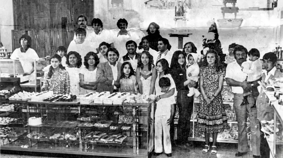 El equipo y la familia de Pasteles Toluca posando tras los mostradores el día de la apertura de la sucursal Juárez, en los años setenta. Fotografía en blanco y negro.
