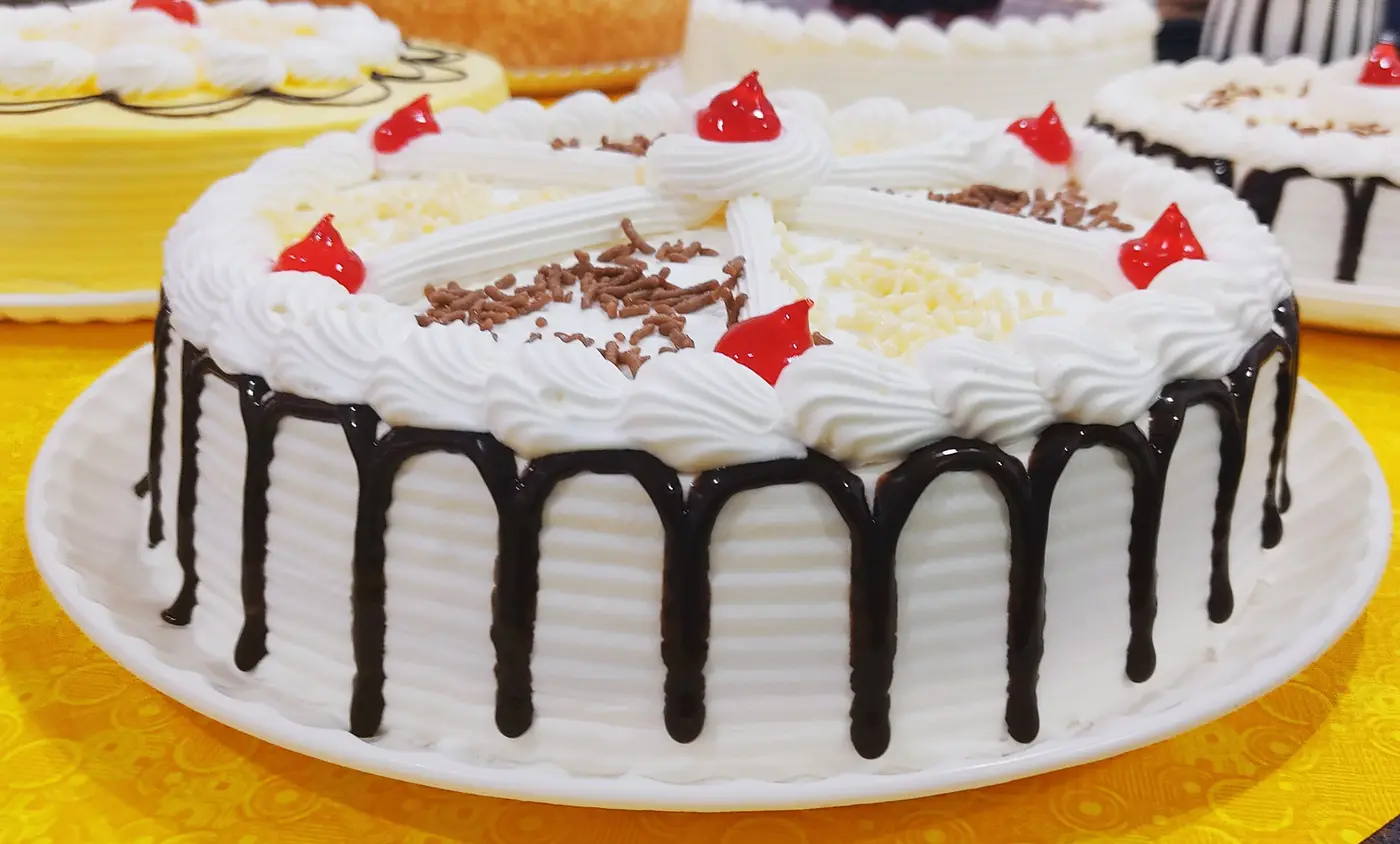 Pastel de tres leches recién decorado, con chorreado de chocolate, cerezas y granillo